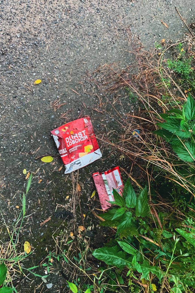 Farbe im Zwiegespräch - Hier nimmt die Verpackung eines Schokoriegels gekonnt und viel Leichtigkeit das Rot des Tetrapacks auf. Der Komplementärkontrast zwischen dem Rot des Mülls und dem Grün der Pflanzen am Wegesrand scheint rein zufällig gesetzt. Doch nur zu leicht übersieht man hier die strenge Anordnung der Bildelemente.